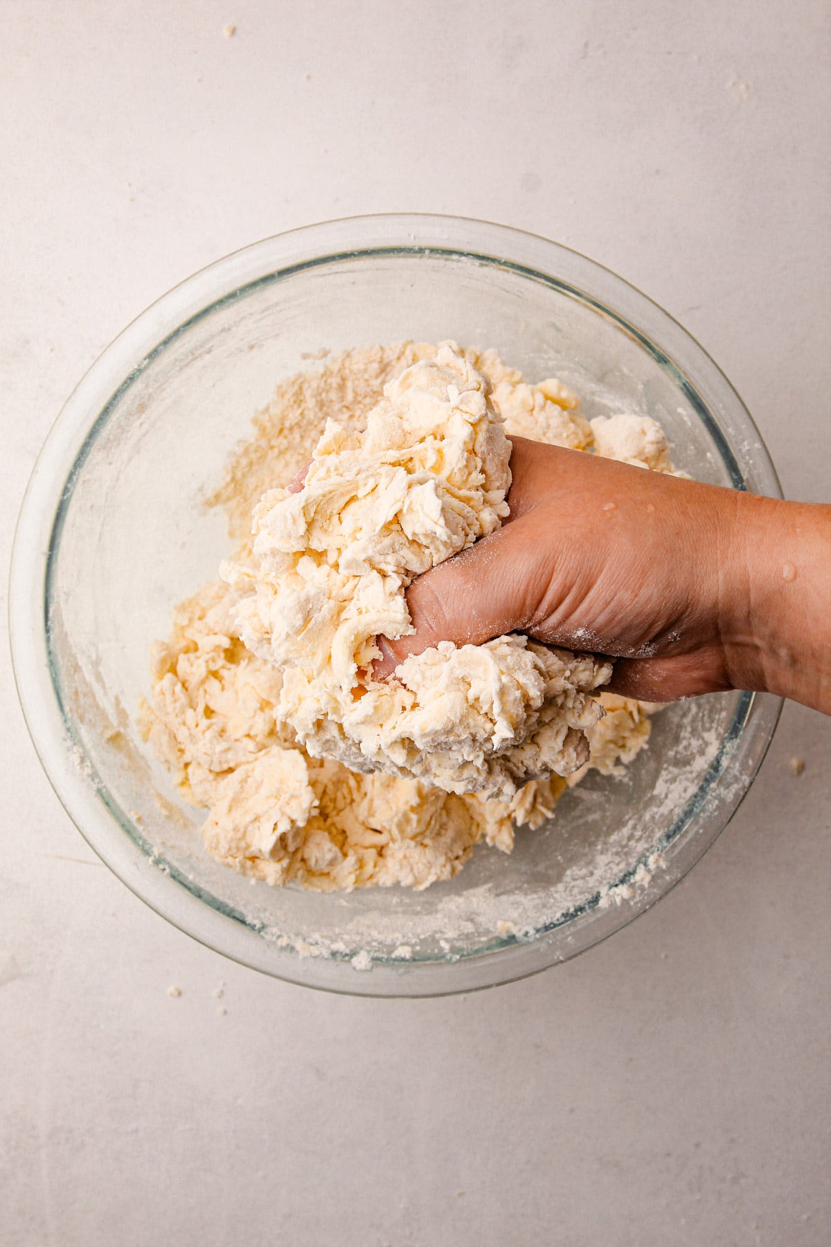 One hand squishing together a mixture of flour and butter over a large bowl