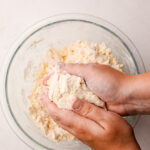 Two hands holding a ball of pie dough over a bowl with more flour and butter in it