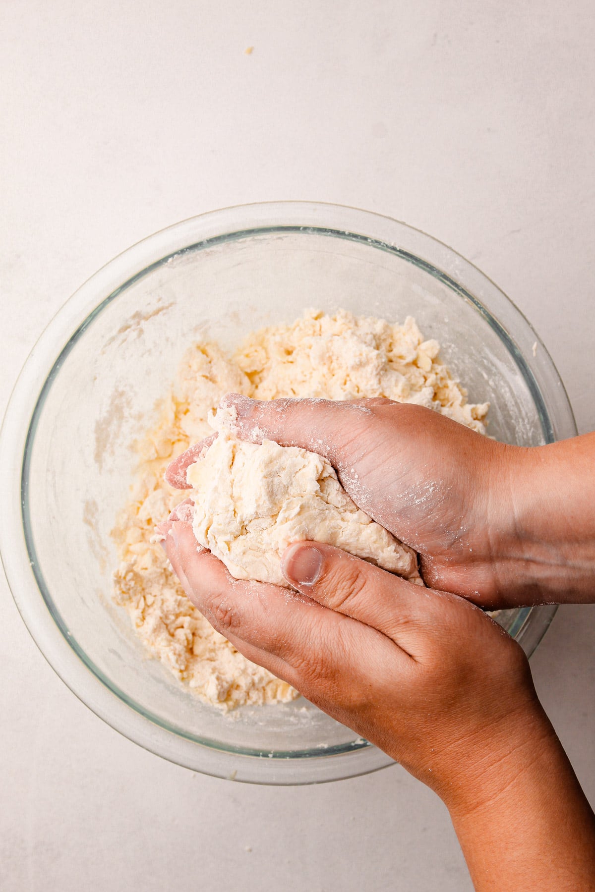 Two hands holding a ball of pie dough over a bowl with more flour and butter in it