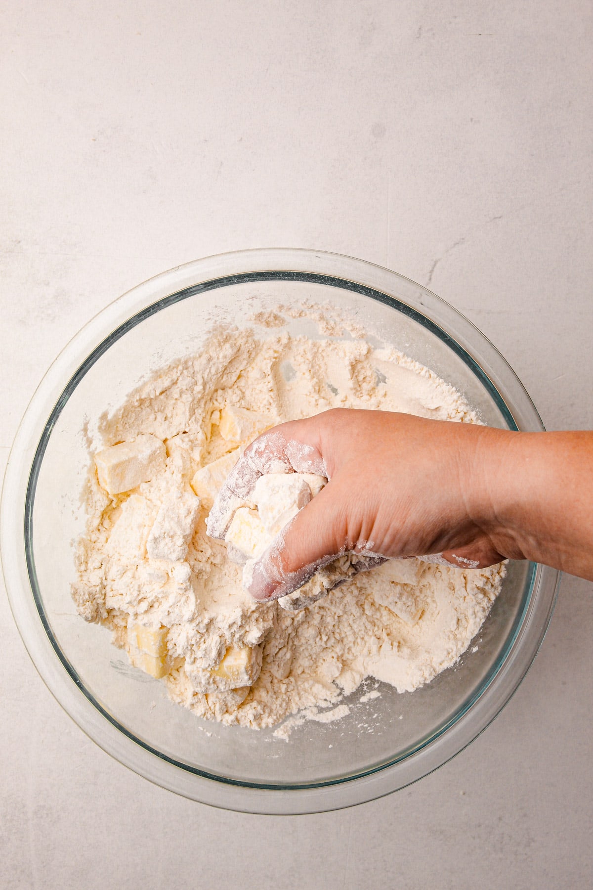 A hand holding cubes of butter covered in flour over a bowl with more flour and butter in it