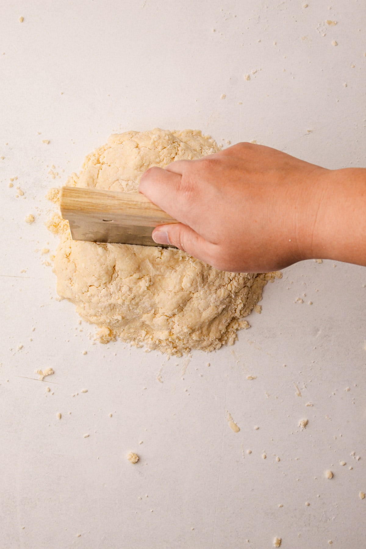 A hand using a bench scraper to cut a mound of pie dough in half on a counter surface