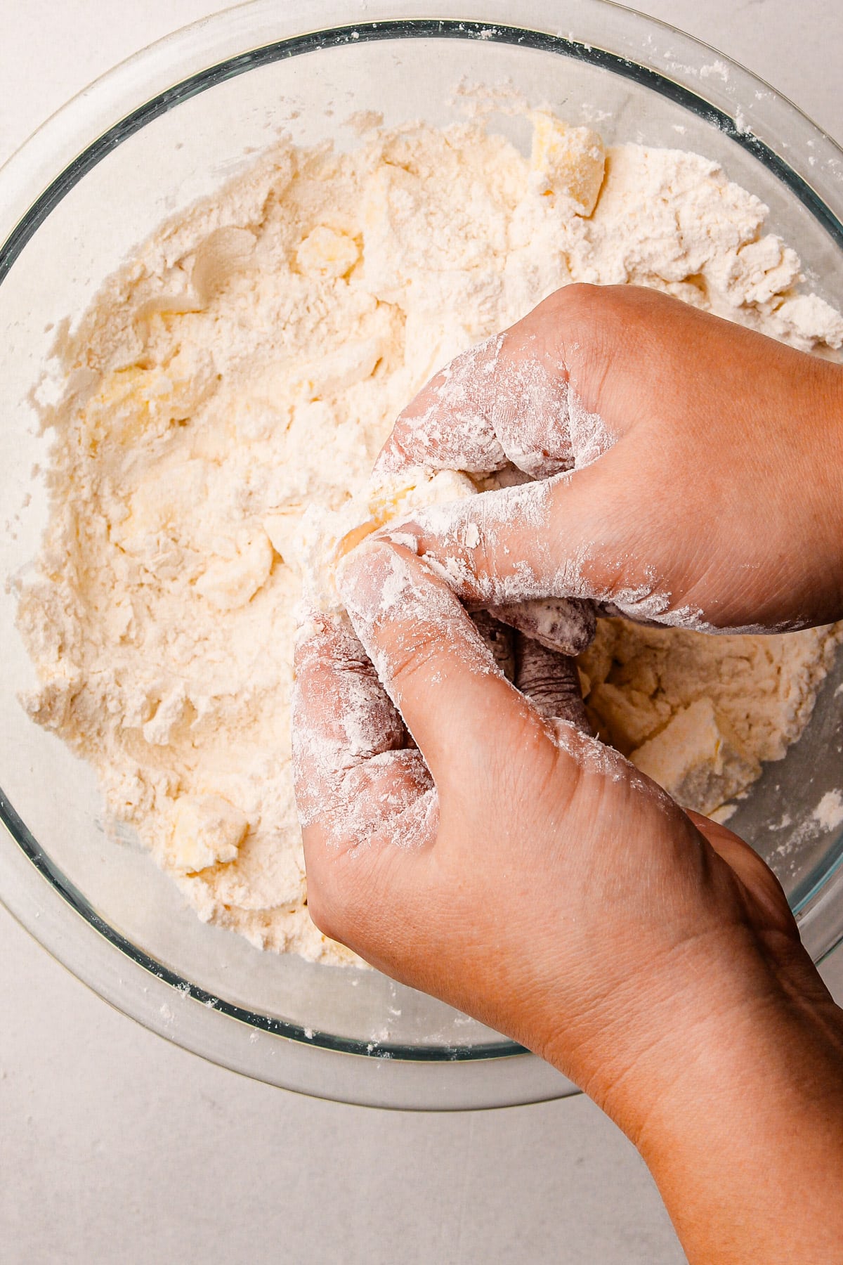 Two hands rubbing flour and butter together over a bowl with more flour and butter in it