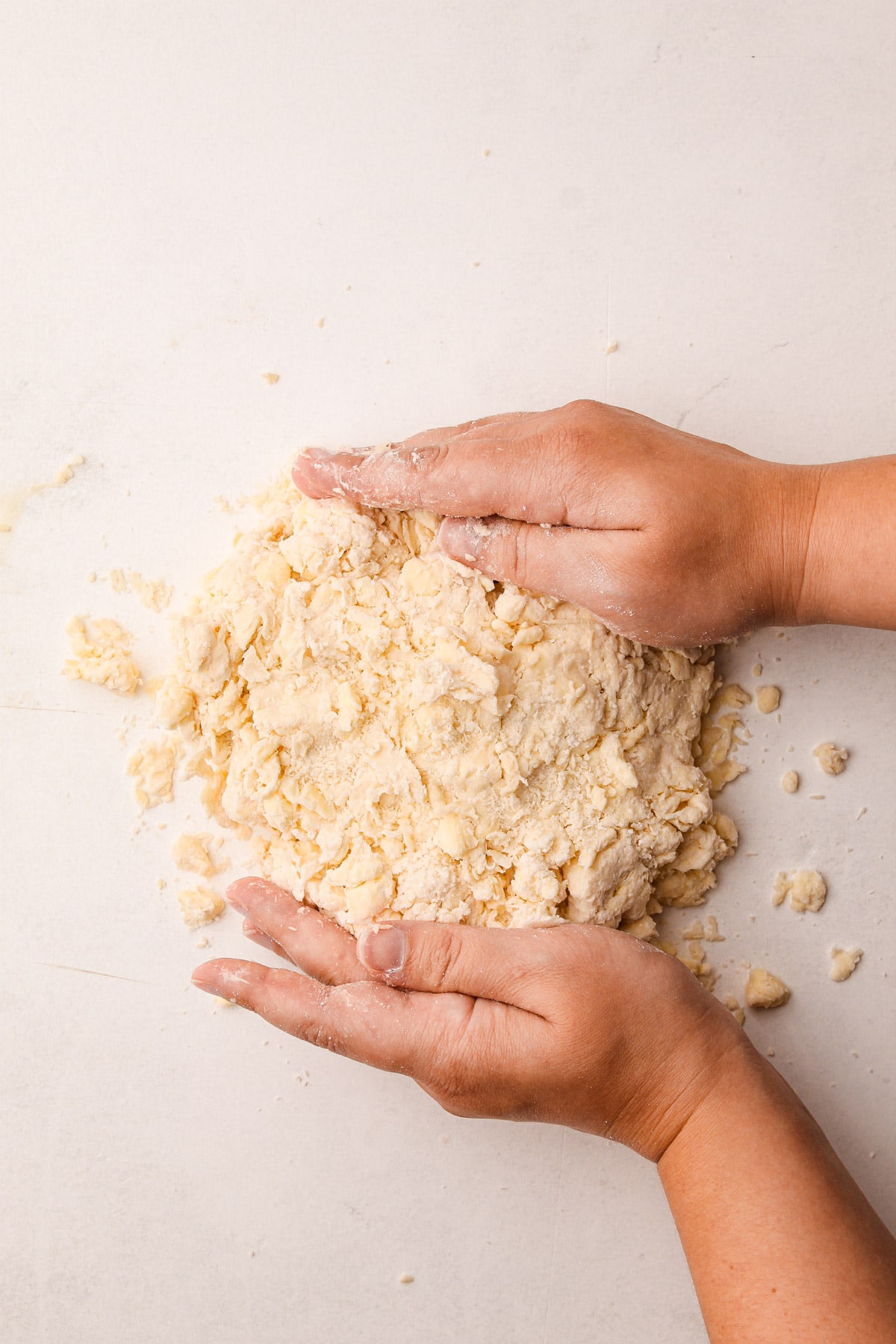 Two hands pushing together a mound of a butter-flour mixture on a counter surface