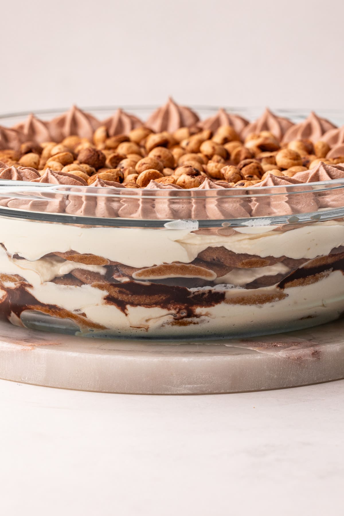 A side view of a finished cookie icebox cake to in a see-through dish to reveal some of the layers of cream, cookies and chocolate sauce.