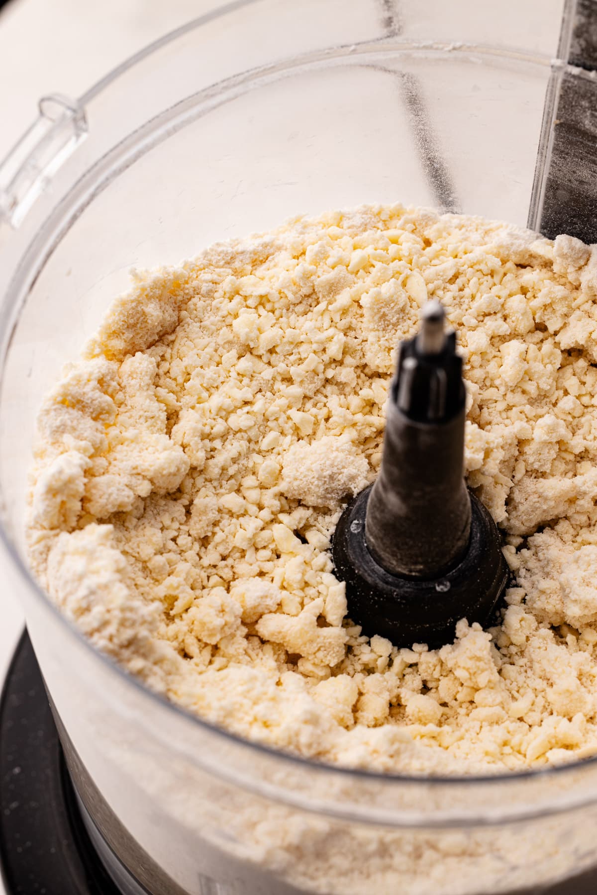 A crumbly mixture of flour and butter in the bowl of a food processor