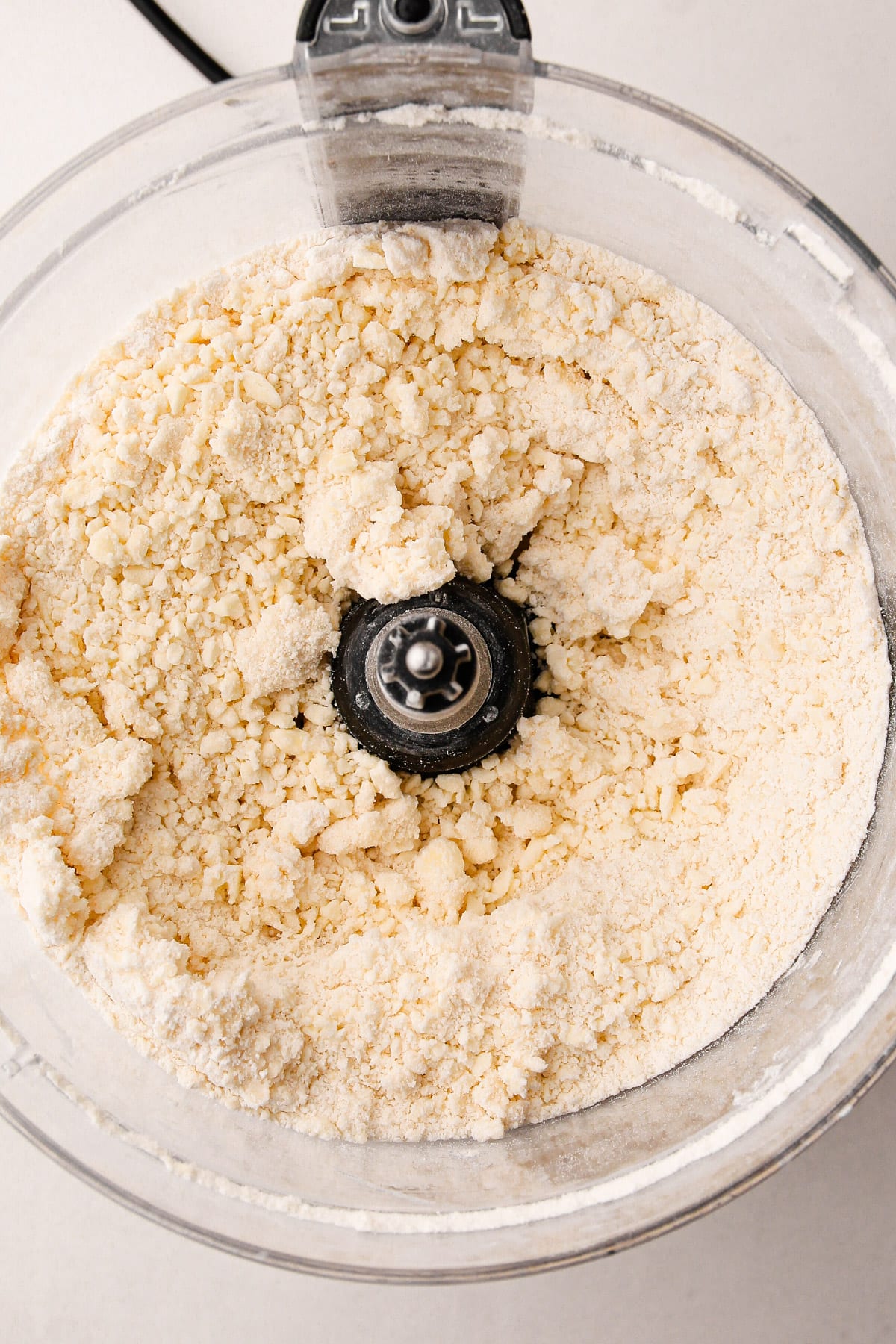 A crumbly mixture of flour, butter and water in the bowl of a food processor