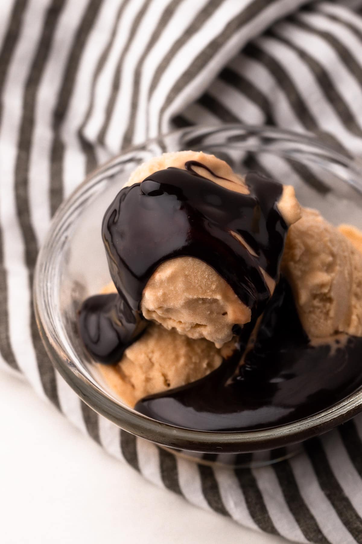 A bowl with scoops of peanut butter ice cream and hot fudge sauce on top, with a striped cloth in the background