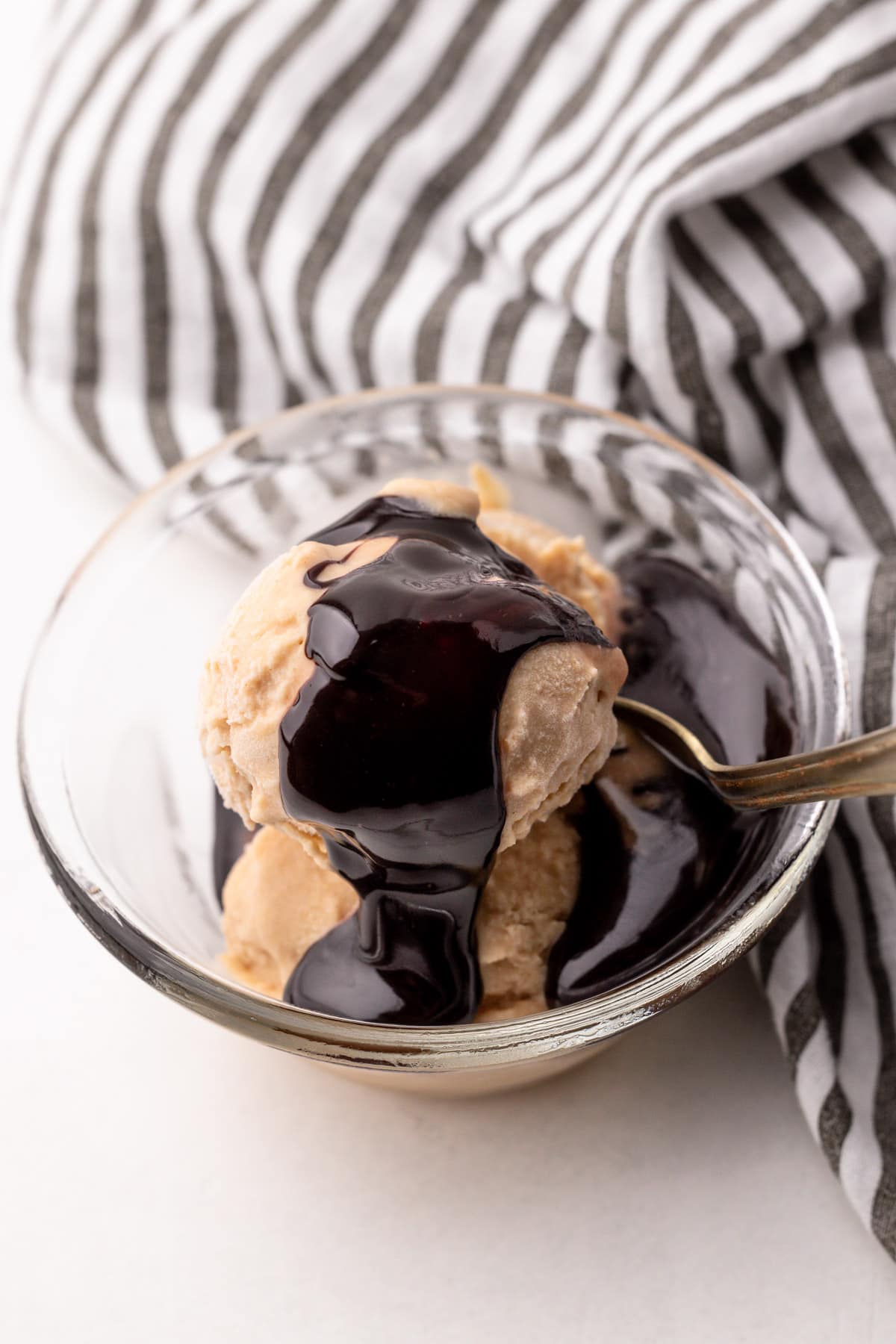 A bowl with scoops of peanut butter ice cream and hot fudge sauce on top, with a striped cloth in the background