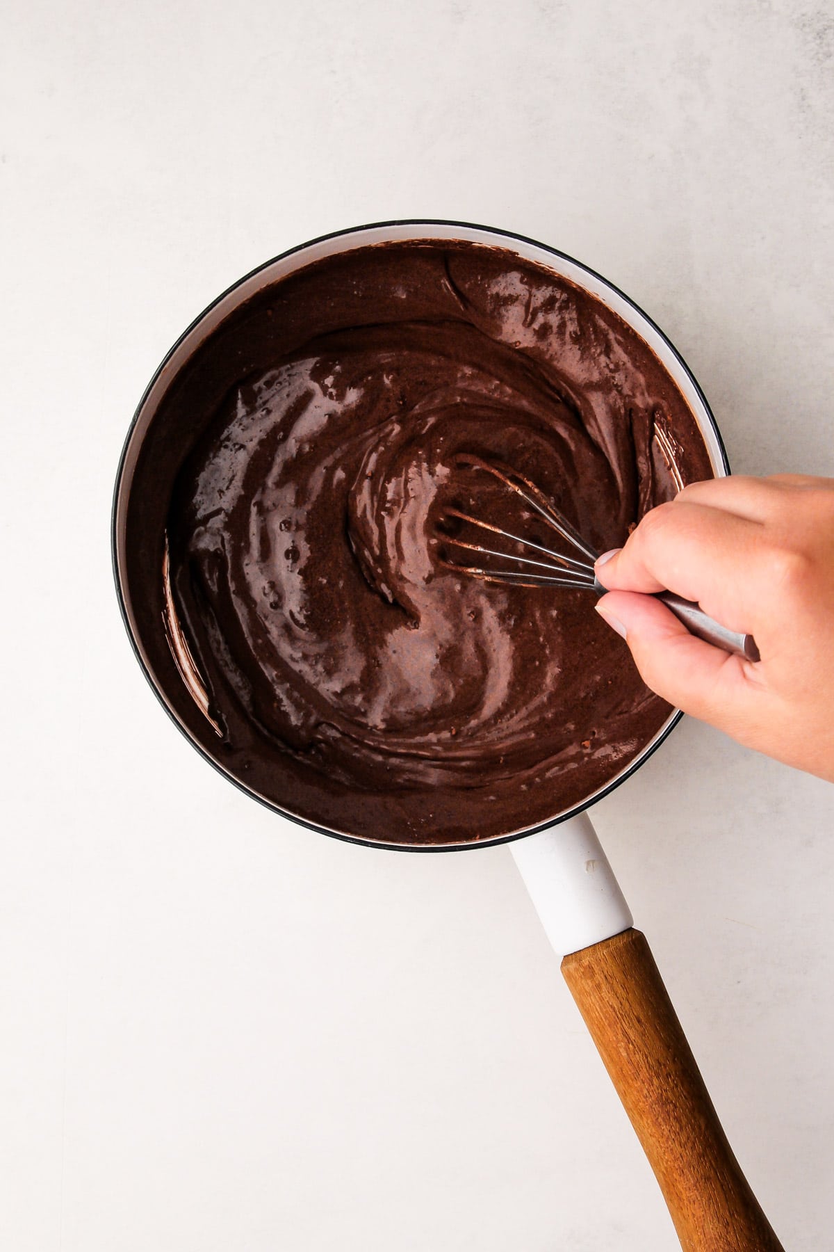 A hand whisking together a cocoa and cream mixture in a pot