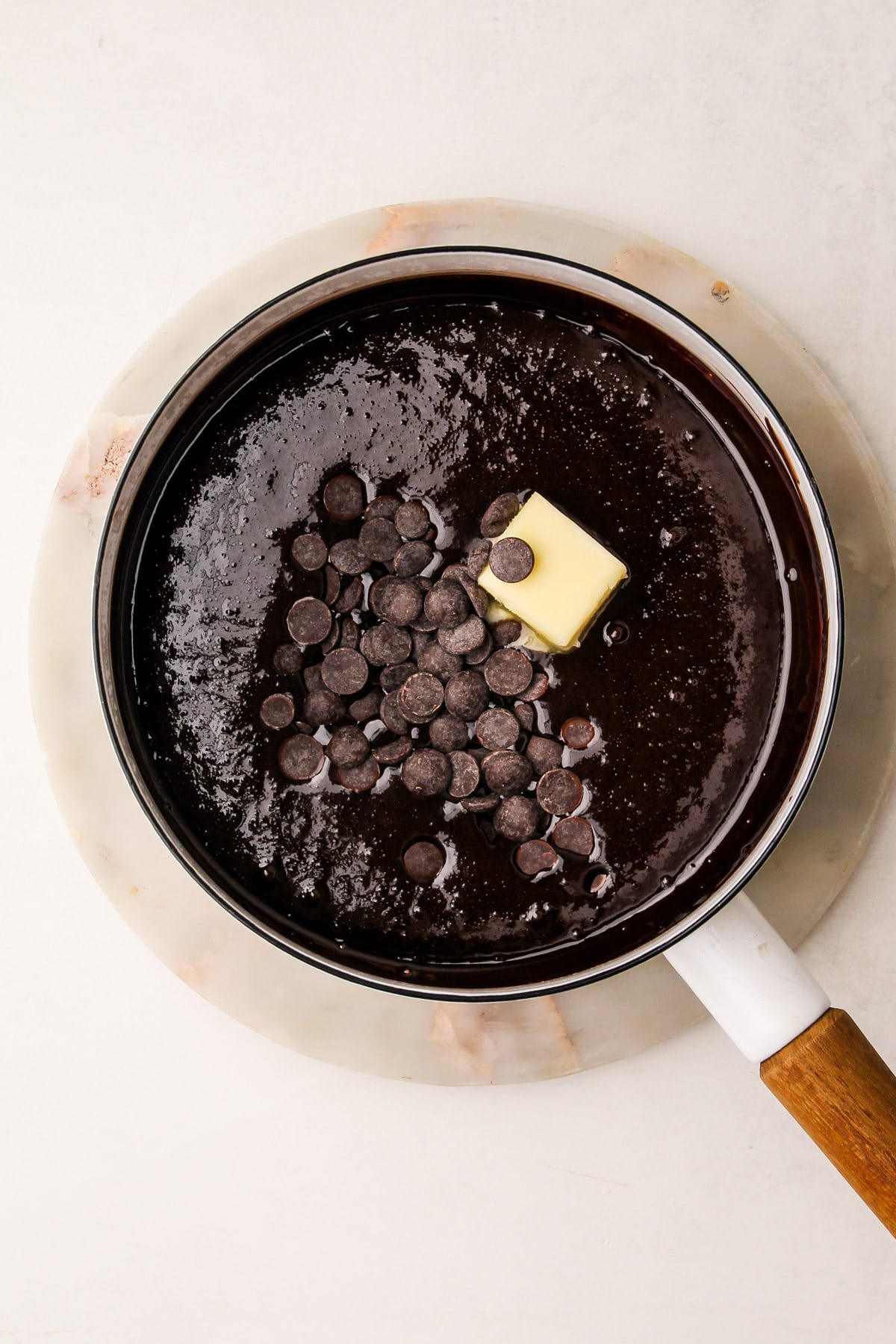 A cocoa mixture in a pot, with chocolate chips and butter added on top of the mixture