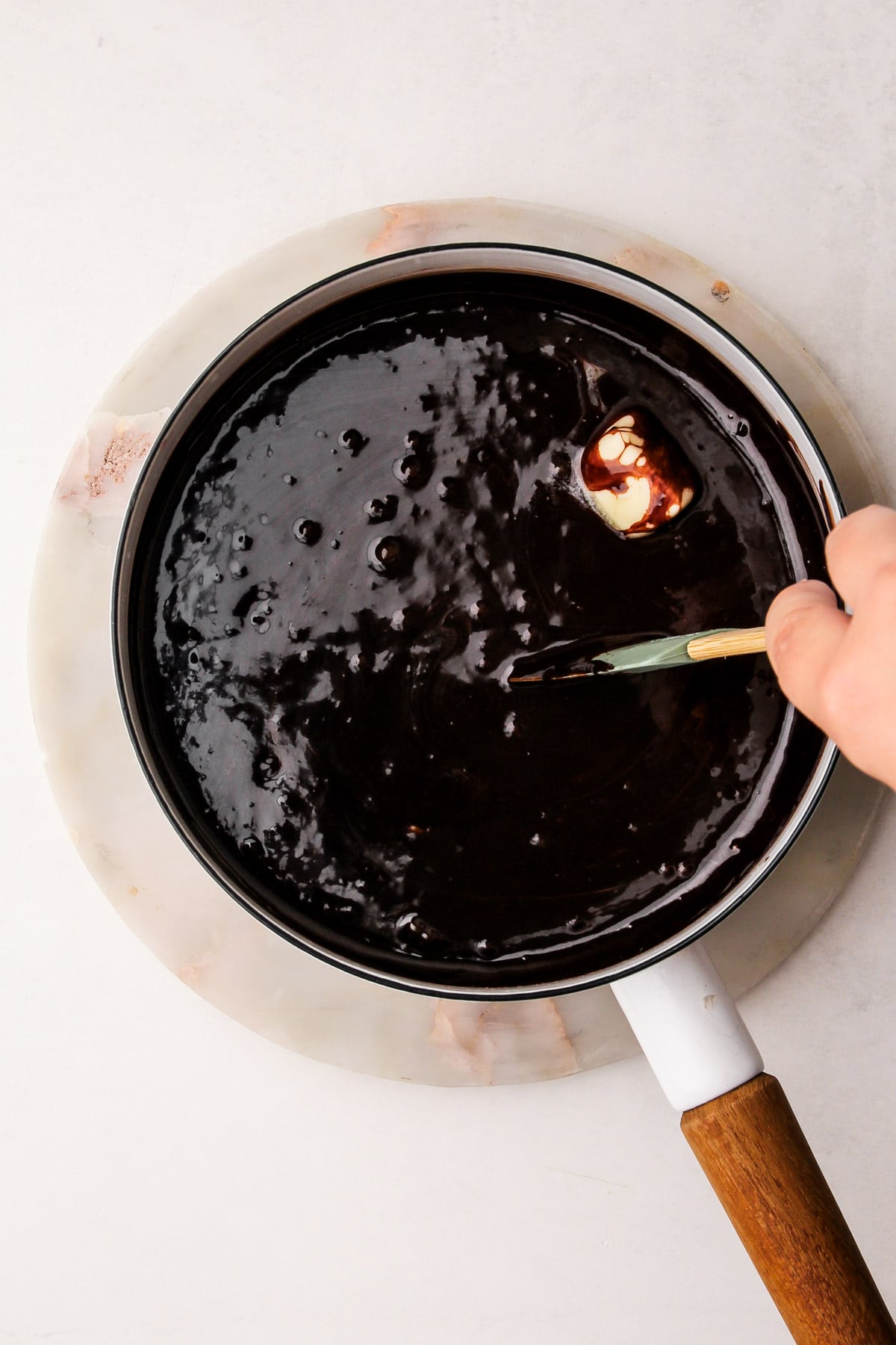 A hand using a rubber spatula to stir together a cocoa mixture, chocolate, and butter together in a pot