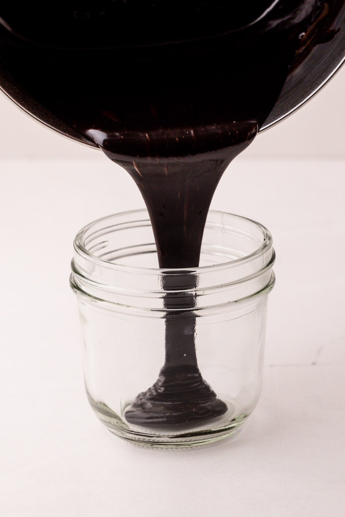 Hot fudge sauce pouring from a pot into a small glass jar