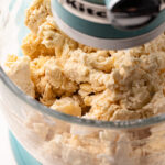 A mixture of flour and butter being mixed together in the bowl of a stand mixer