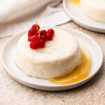 A vanilla bean panna cotta dessert on a white plate with lemon curd and red berries.