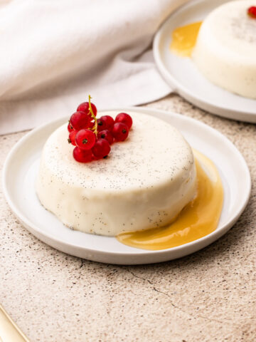 A vanilla bean panna cotta dessert on a white plate with lemon curd and red berries.