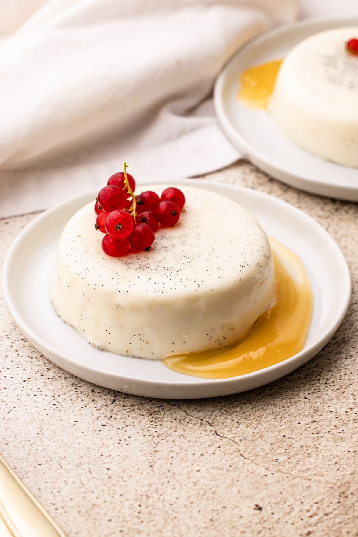 A vanilla bean panna cotta dessert on a white plate with lemon curd and red berries.