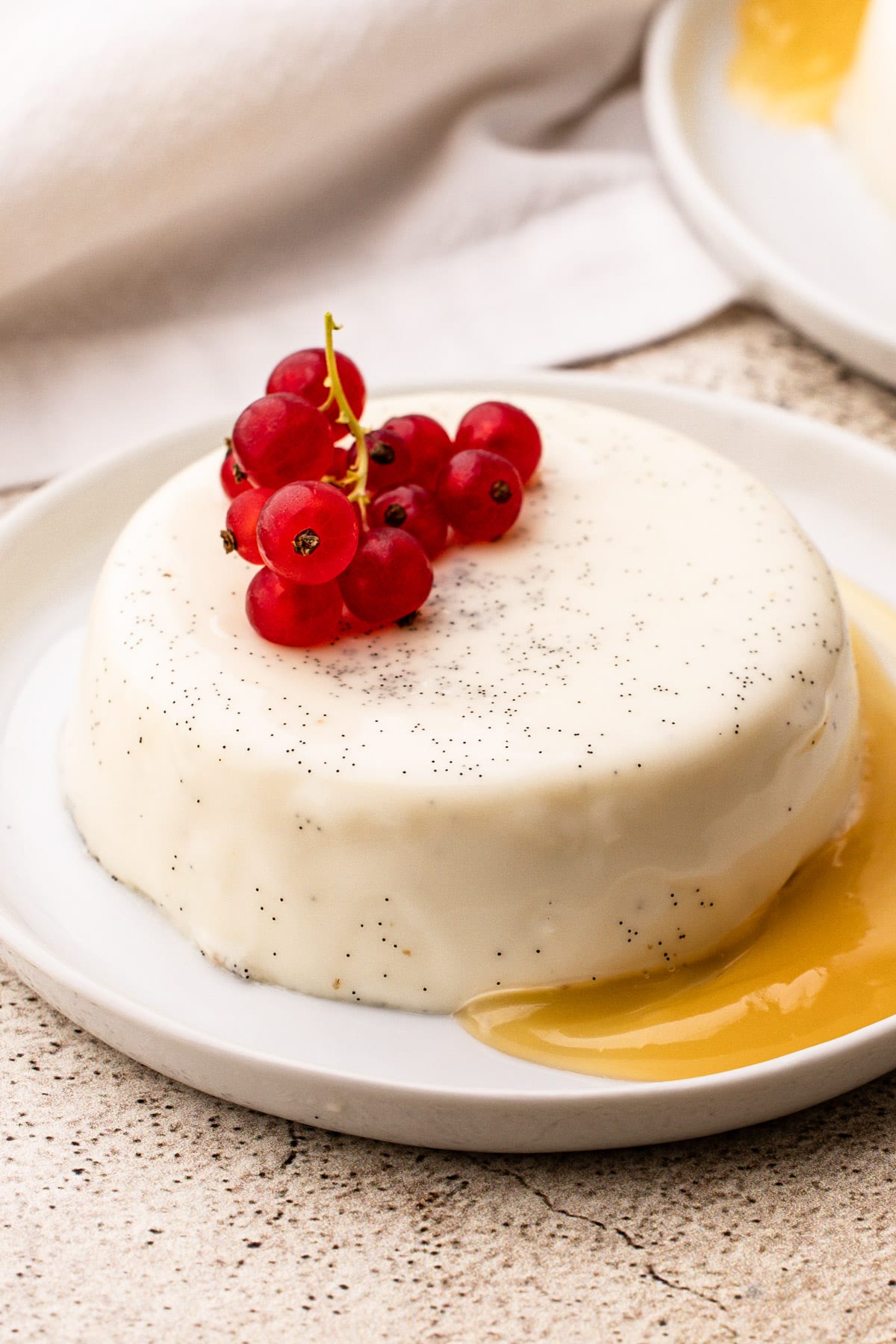 Panna cotta on a plate with a ton of visible vanilla beans in the custard dessert on a white plate with lemon curd and red berries.