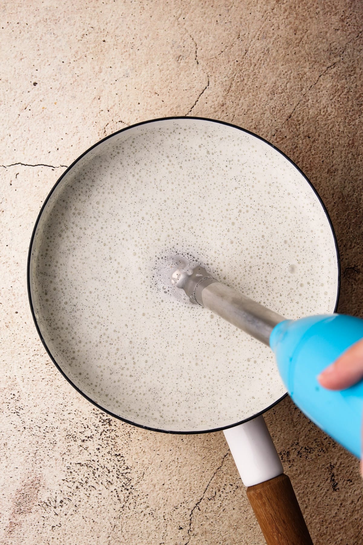 A pot with vanilla bean panna cotta being mixed together with an immersion blender.