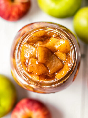 A jar of precooked appie pie filling surrounded by fresh apples.