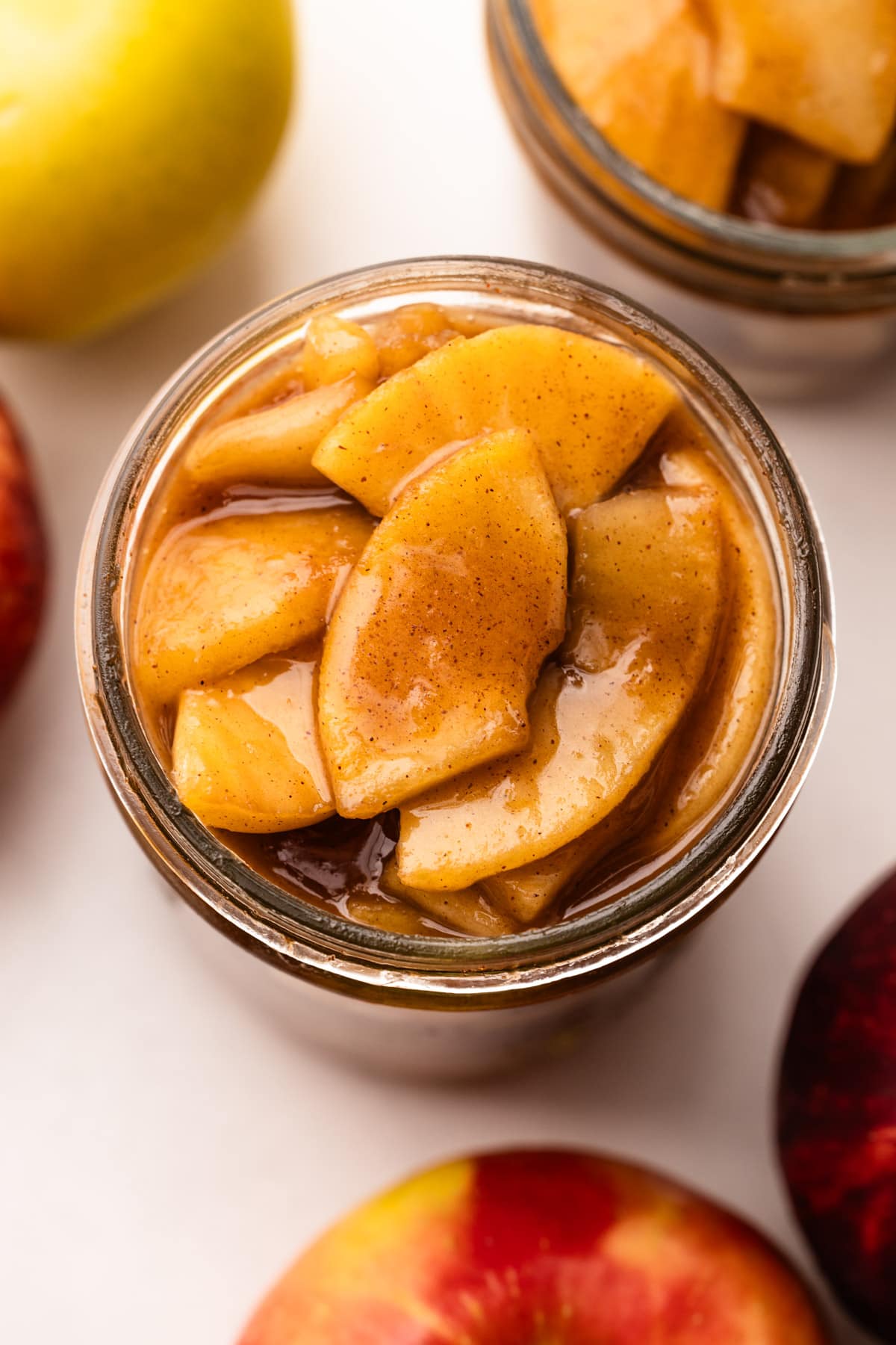 A jar filled to the top with apple pie filling surrounded by apples.