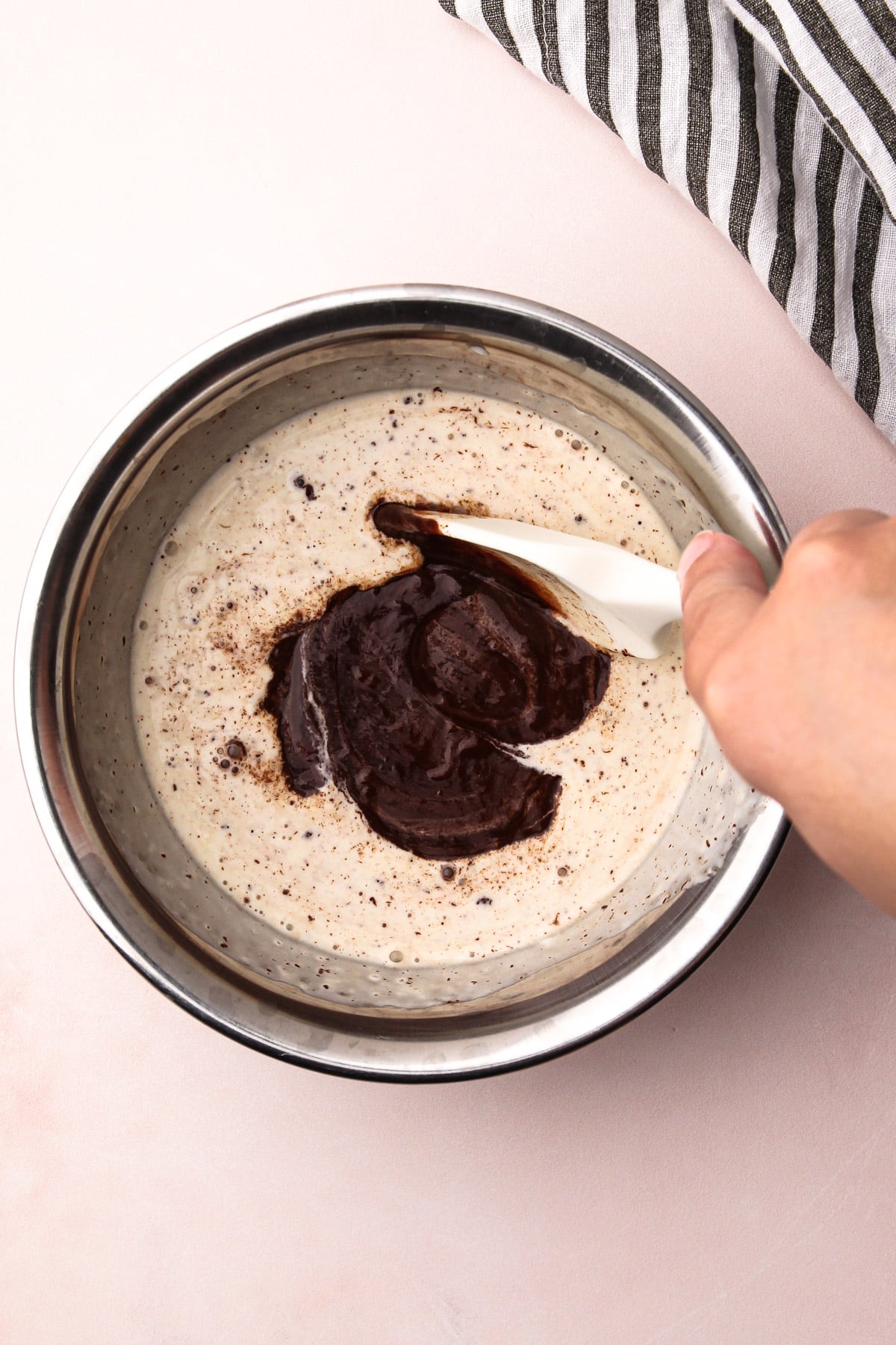 A hand stirring together melted chocolate and cream in a bowl with a rubber spatula to make chocolate ganache.