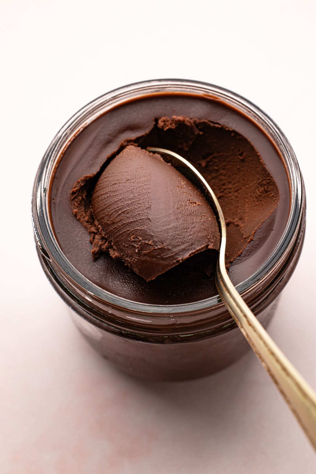 Thickened chocolate ganache sauce being scooped from a glass jar with a spoon.