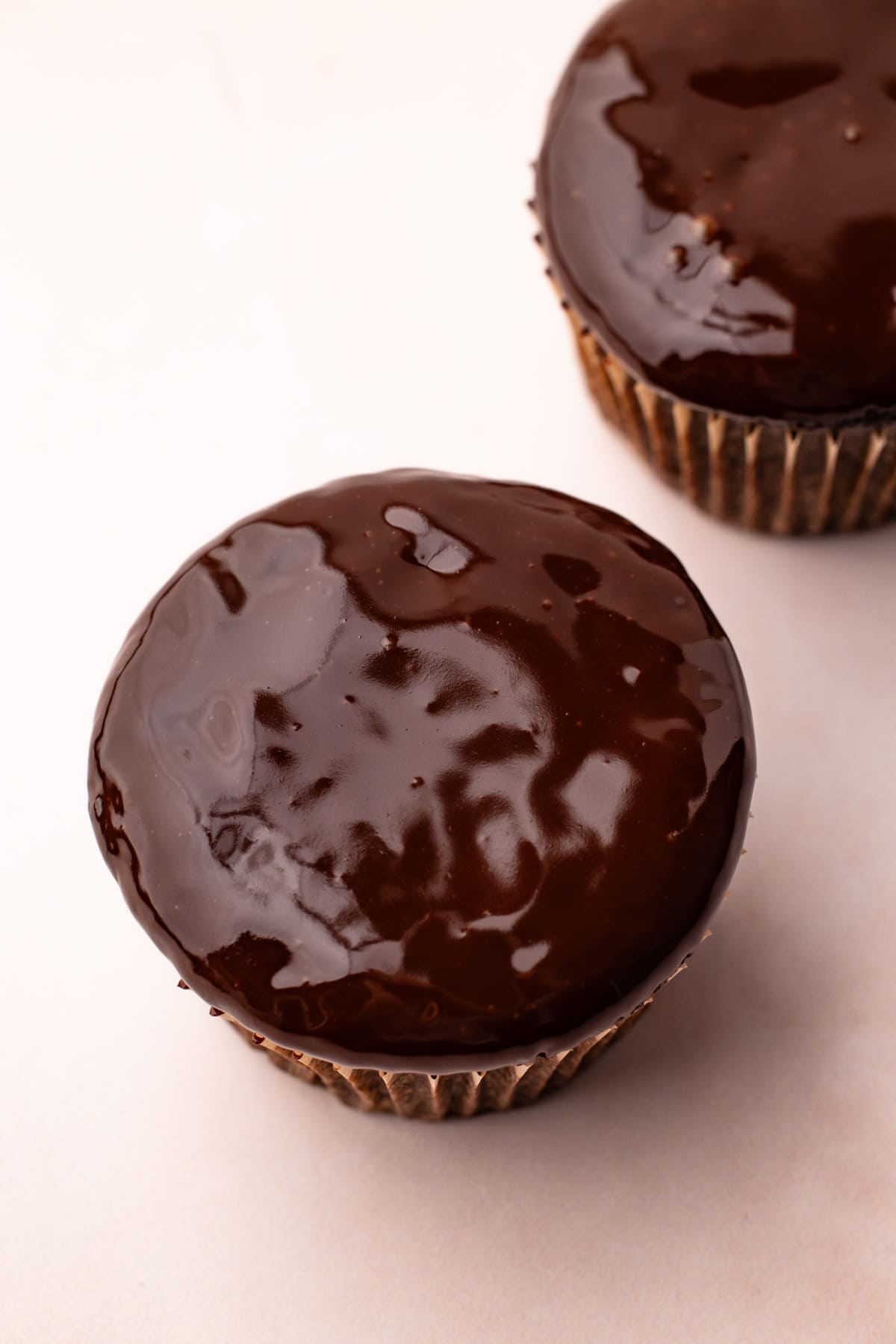Shiny, melted chocolate ganache sauce on top of a chocolate cupcake.