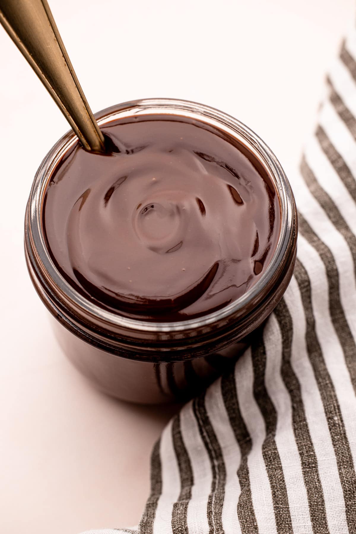 Shiny, melted chocolate ganache sauce in a glass jar with a spoon in it.