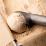 Cinnamon ice cream in a parchment-lined metal loaf tin, with a scoop formed in an ice cream scoop.