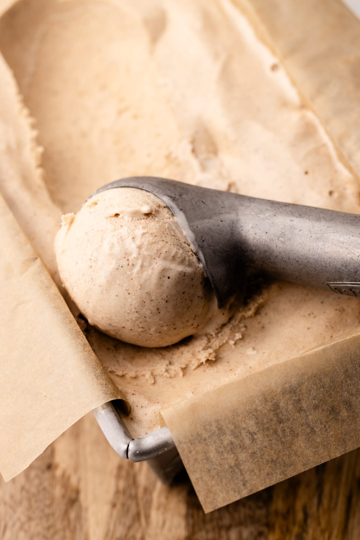 Cinnamon ice cream in a parchment-lined metal loaf tin, with a scoop formed in an ice cream scoop.