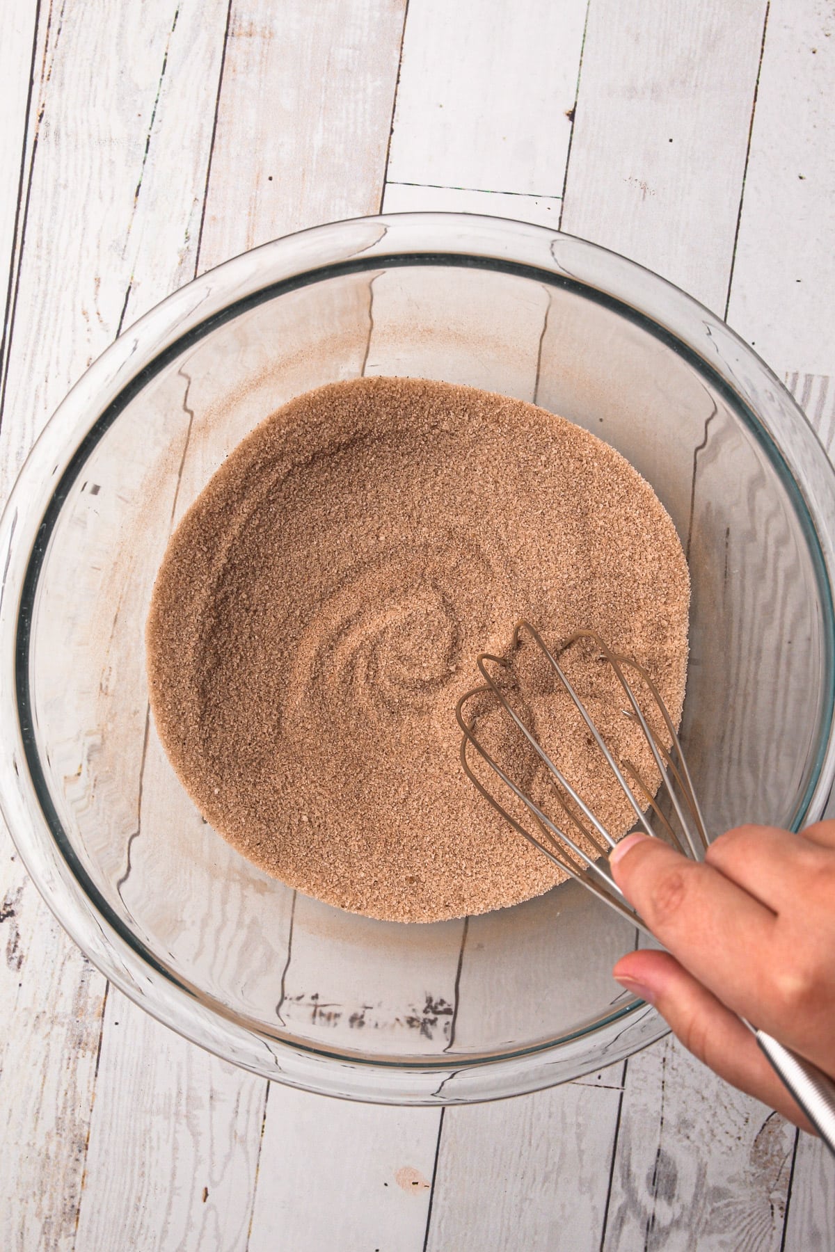 A hand whisking together a cinnamon-sugar mixture in a bowl.