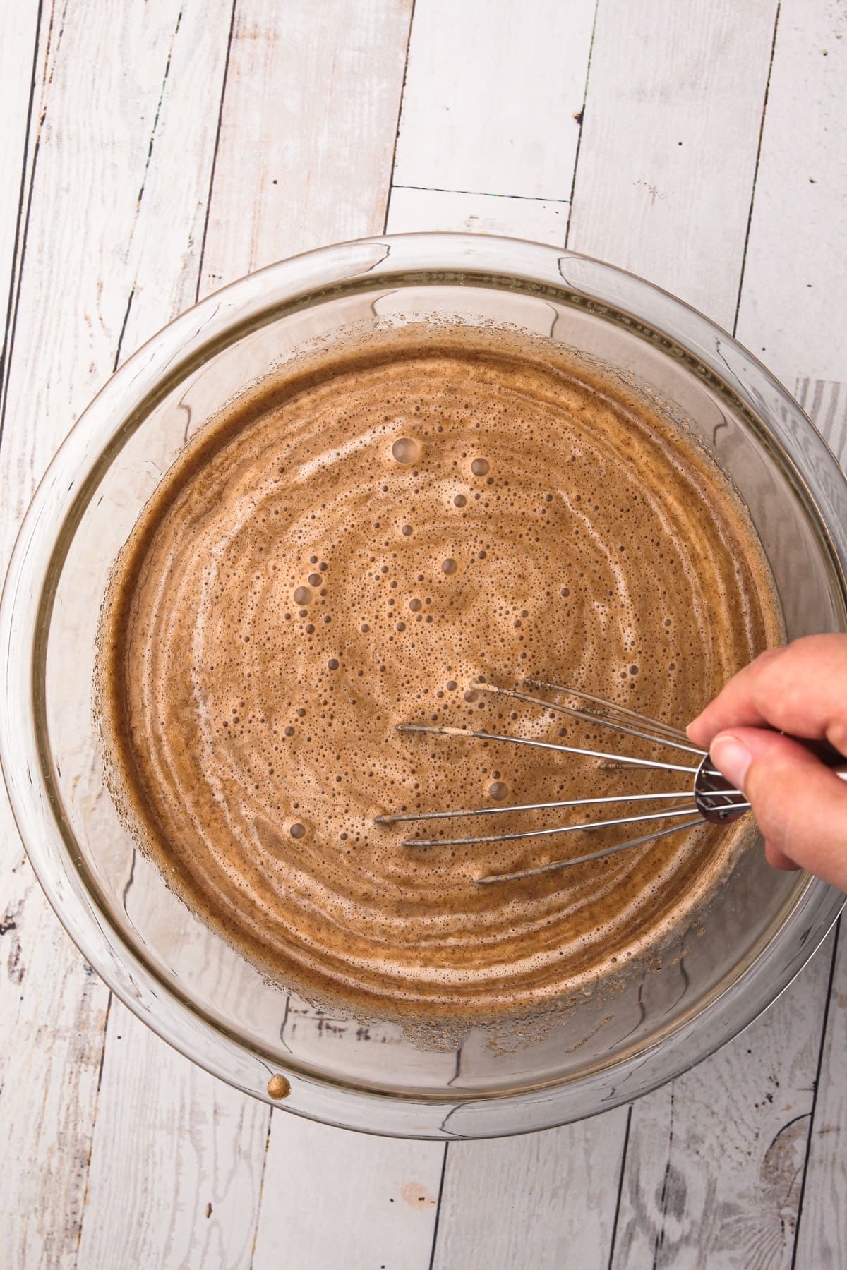 A hand whisking together a cinnamon ice cream base mixture in a bowl.