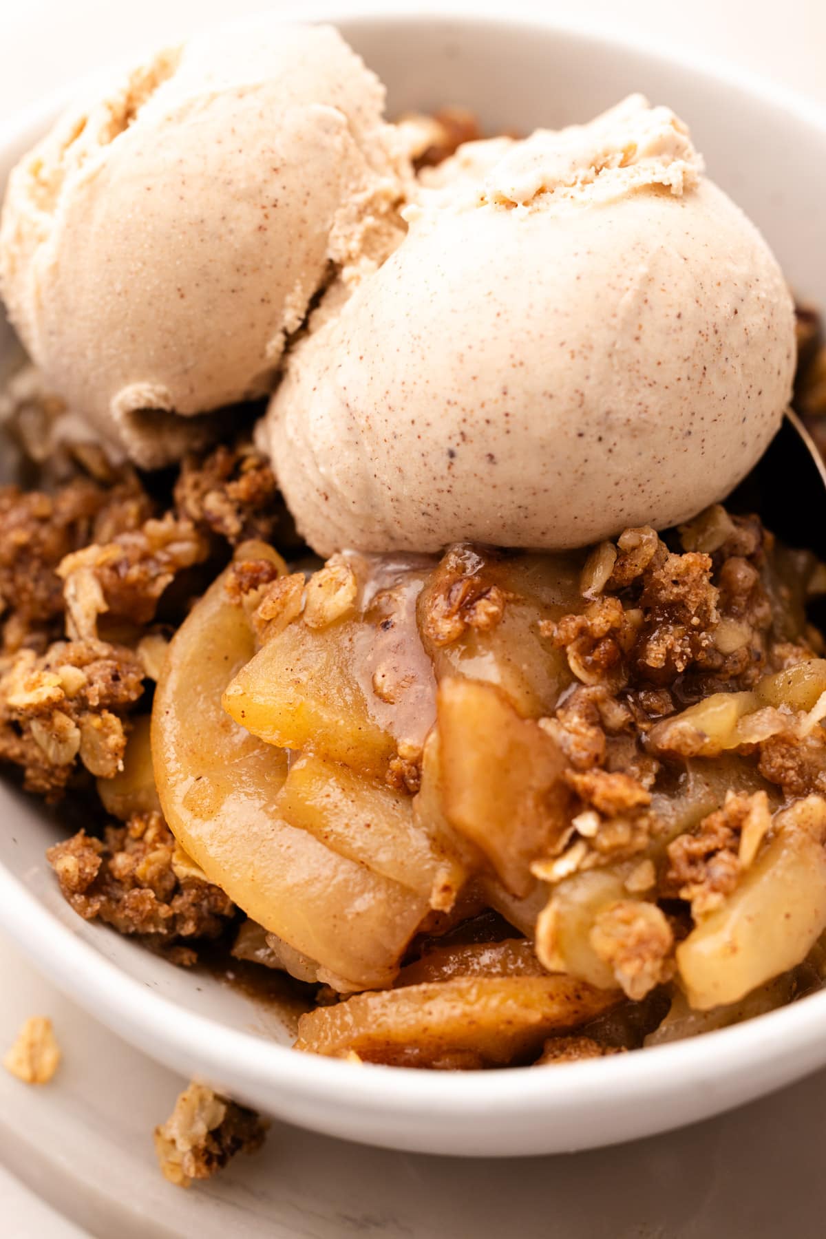 A bowl of baked apple crisp made from wholesome ingredients topped with two scoops of ice cream.