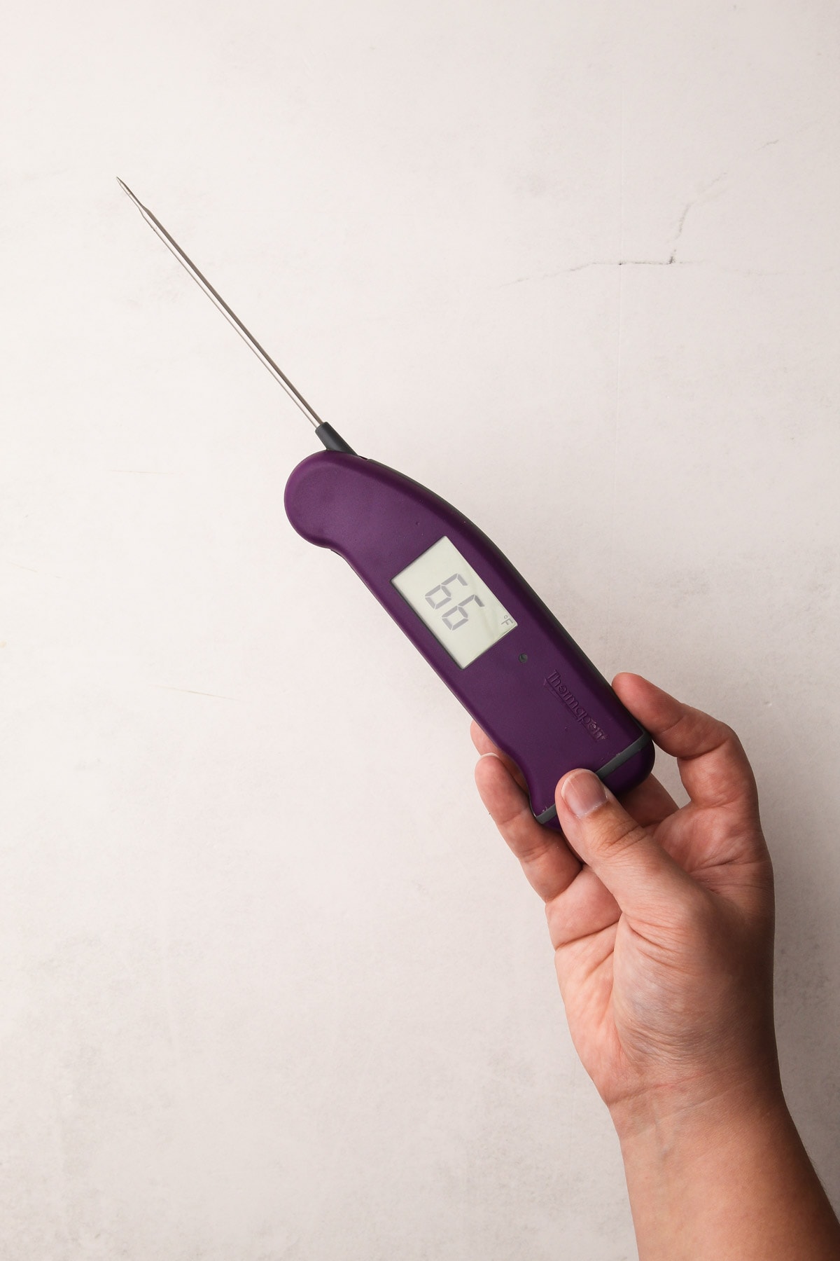 A hand holding an instant-read thermometer, used as a pie baking tool.