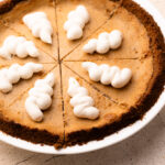 A baked Cinnamon Pie, topped with piped whipped cream and cut into slices.