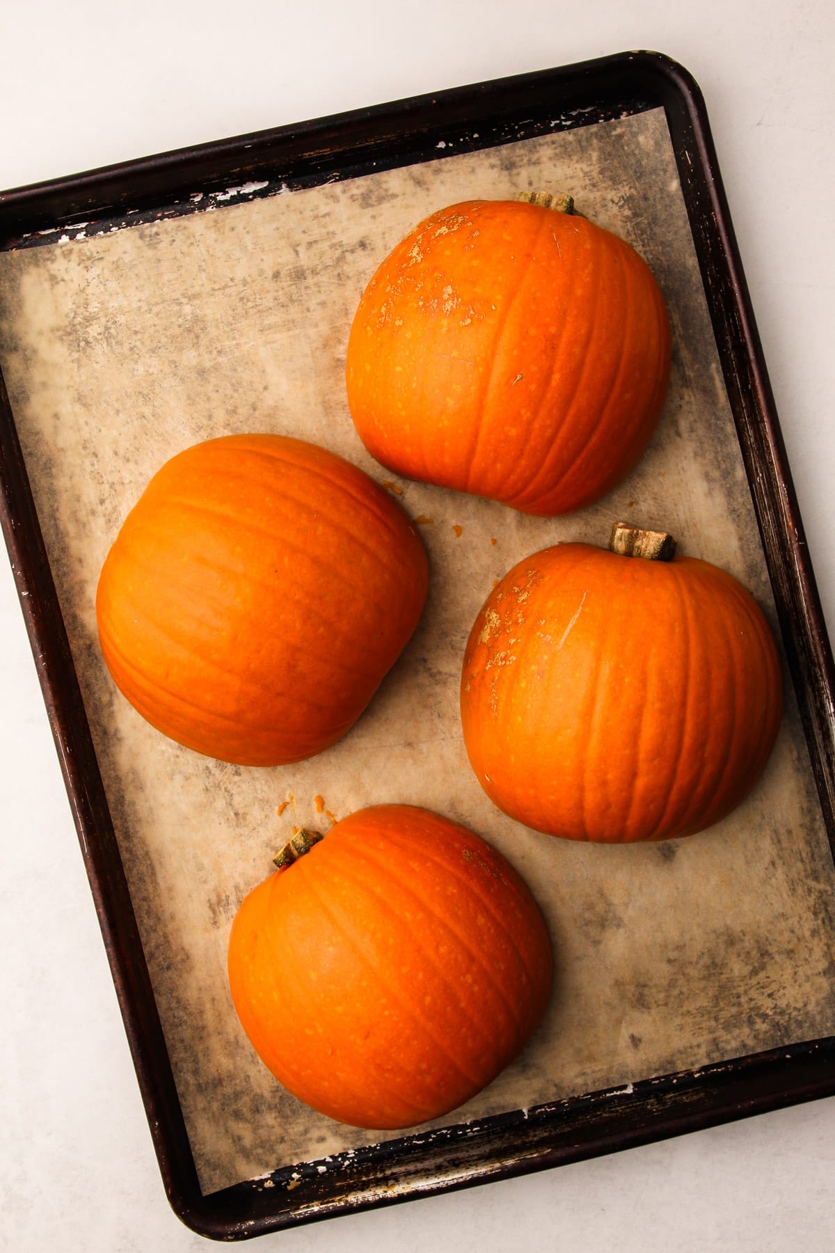 Two sugar pumpkins cut in half on a sheet tray, cut side down.