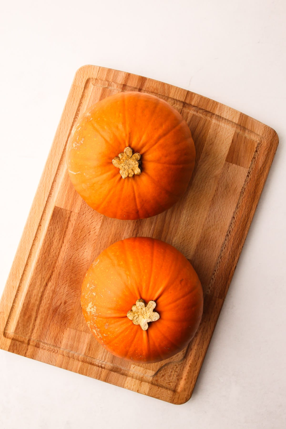 Two clean sugar pumpkins on a cutting board.