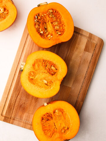 Two sugar pumpkins cut in half on a cutting board.