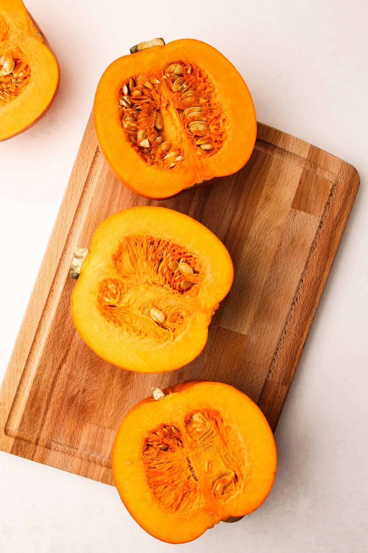 Two sugar pumpkins cut in half on a cutting board.