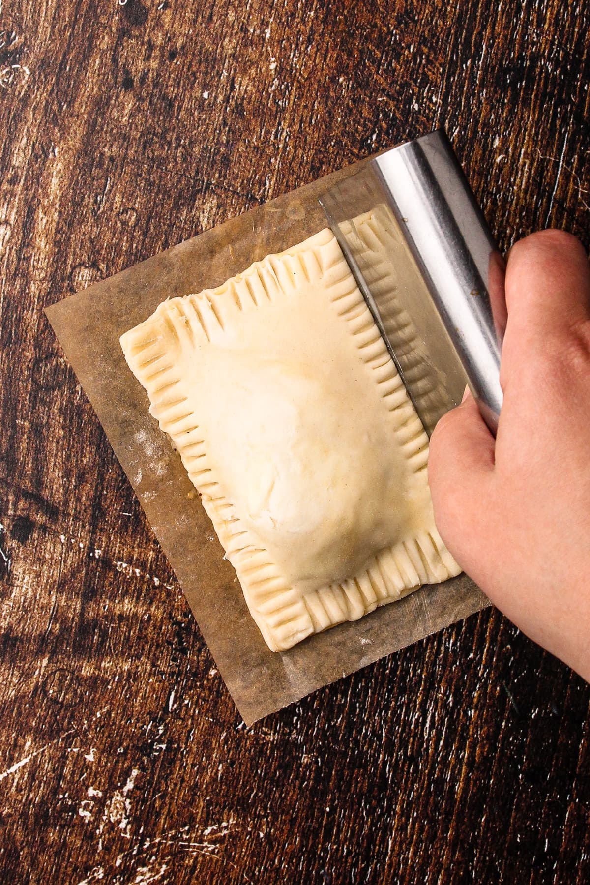 Using a bench scraper to neaten up the edges of an unbaked turkey hand pie.