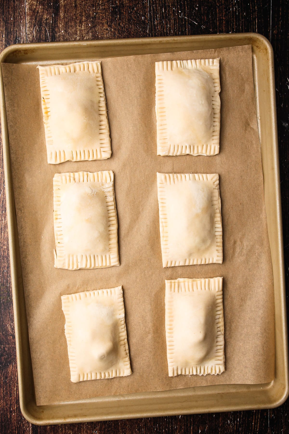 Six assembled turkey hand pies on a baking sheet.