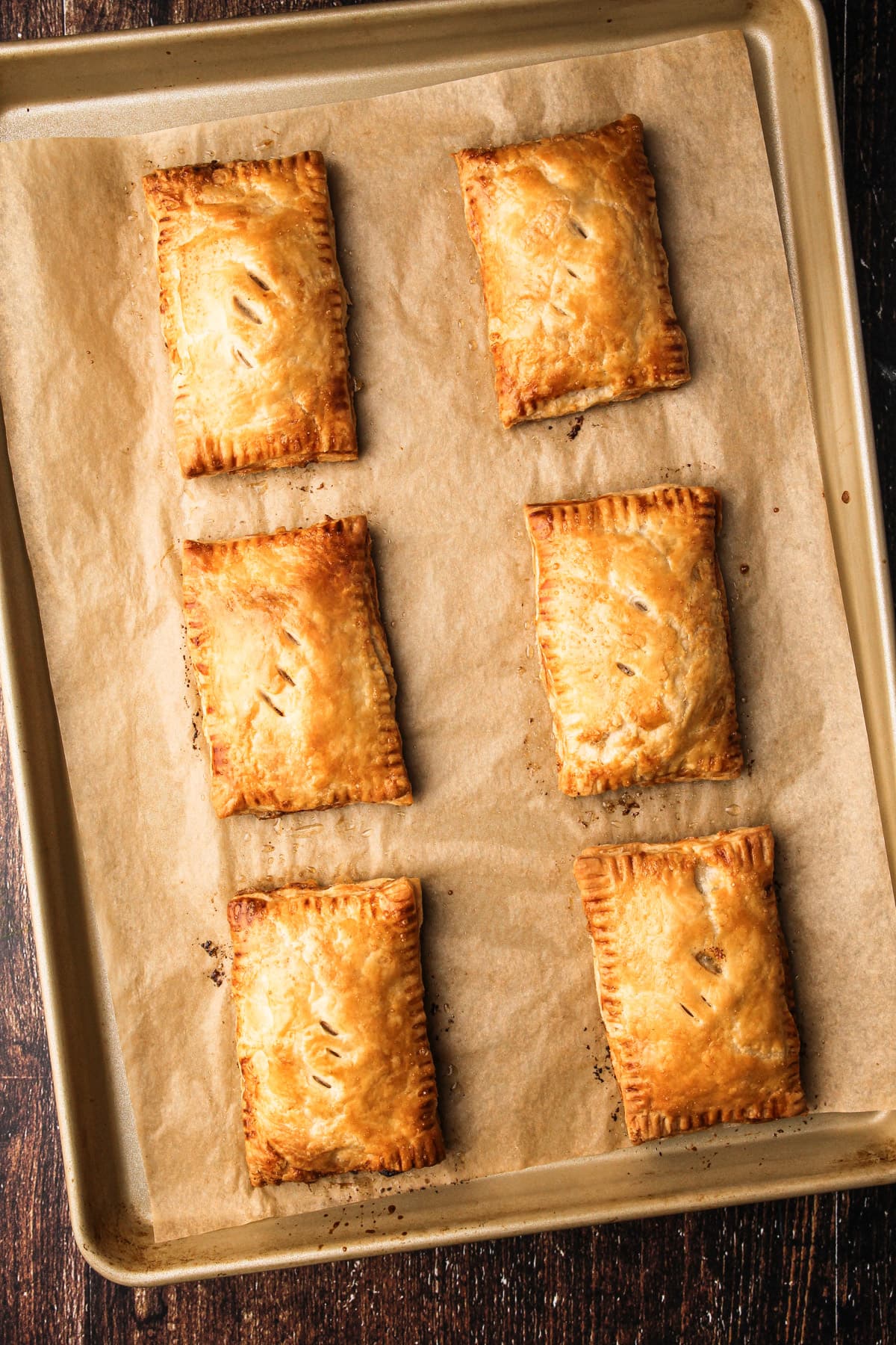 Six baked turkey hand pies on a baking sheet.