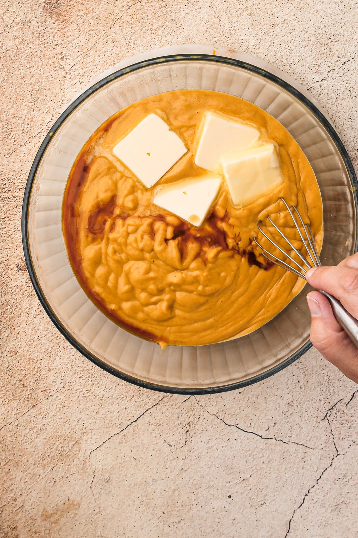 Strained Pumpkin Cream Pie filling in a bowl, with a hand whisking in butter and vanilla.