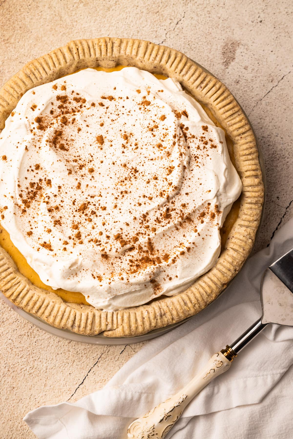 A Pumpkin Cream Pie with whipped cream on top, sprinkled with cinnamon, with a pie server next to it.