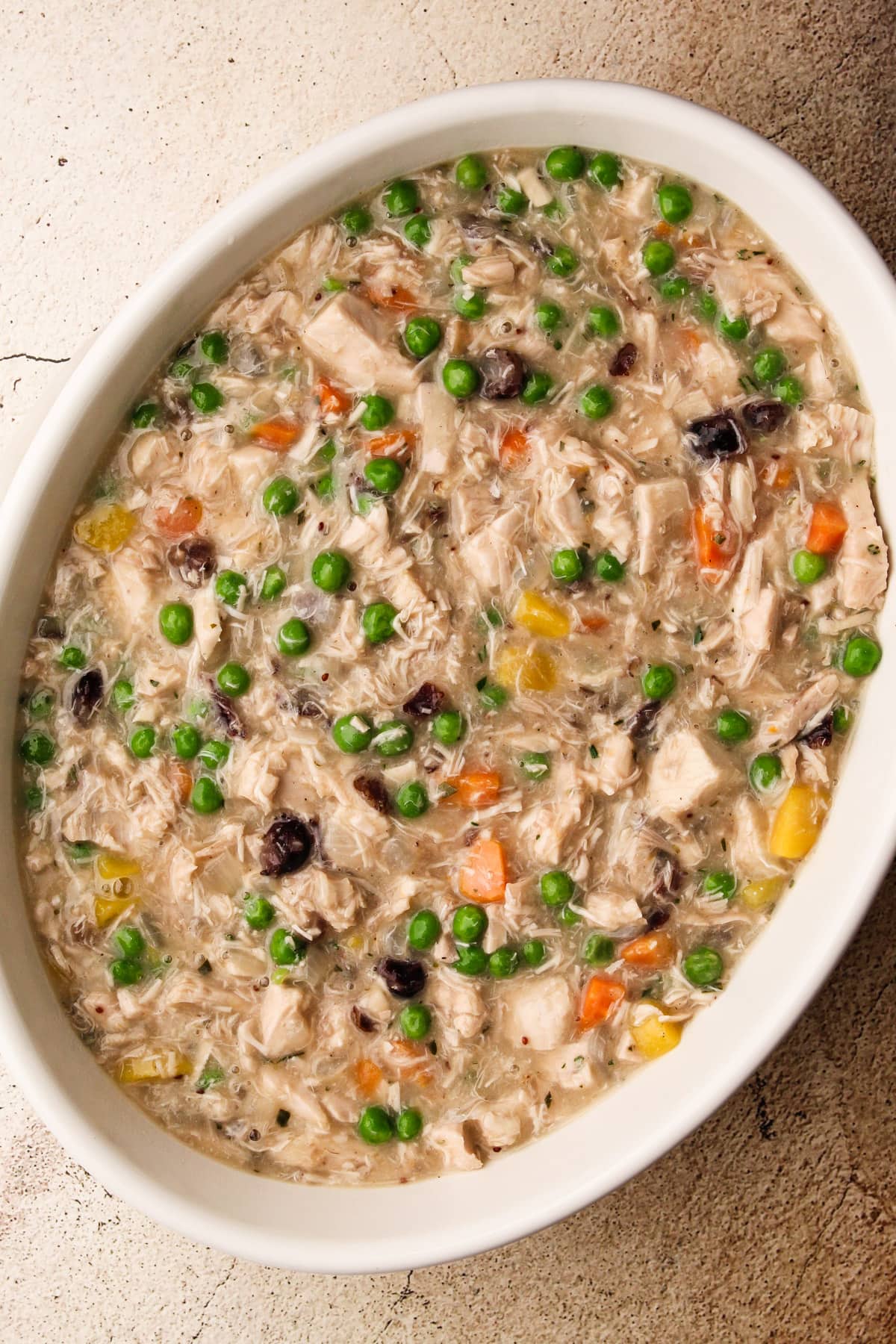 Cooled turkey pot pie filling in a white baking dish.