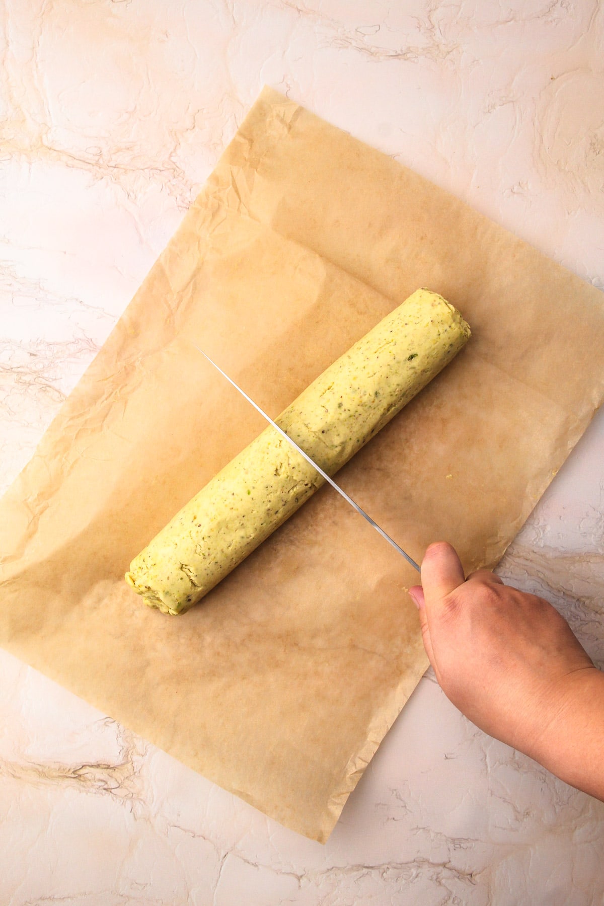 Cutting a chilled pistachio shortbread cookie log in half.