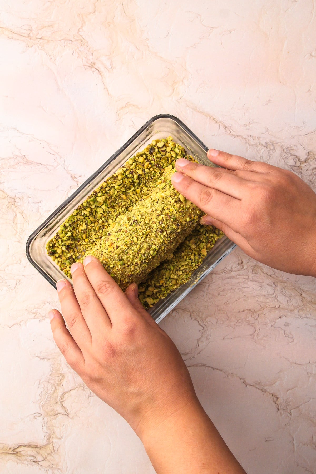 Rolling the pistachio cookie dough log into ground pistachios to coat them.