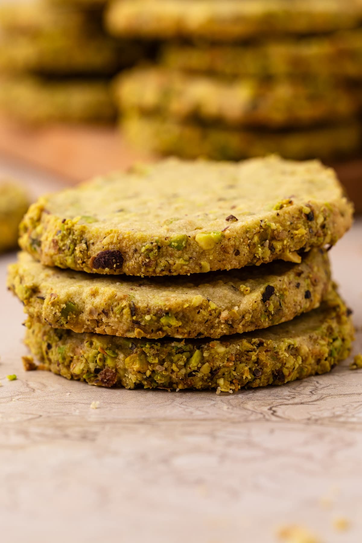 Three pistachio shortbread cookies with fresh pistachios stacked up.