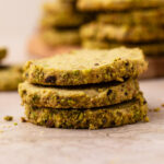 Three pistachio shortbread cookies with fresh pistachios stacked up.