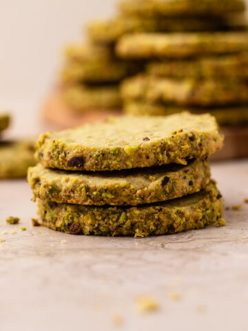 Three pistachio shortbread cookies with fresh pistachios stacked up.